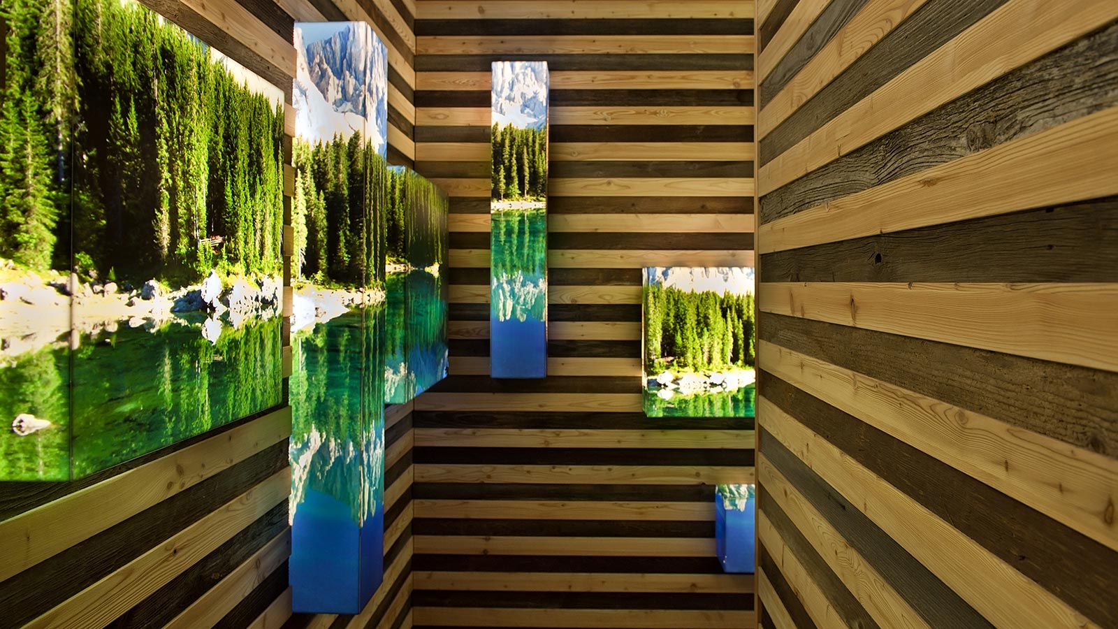 Ein Gang des Hotels, an den Wänden aus Holz hängen leuchtende Bilder der Natur in Moena